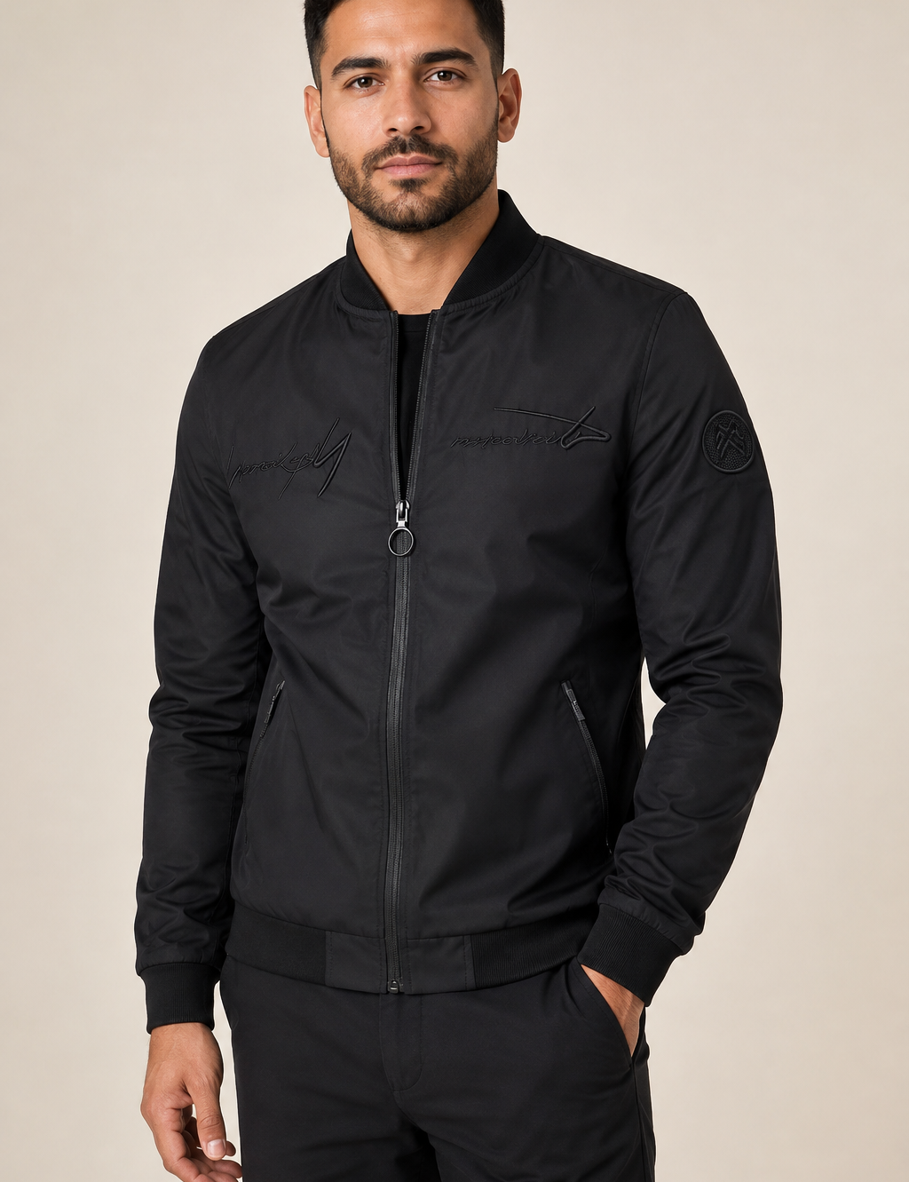 Men's black embroidered bomber jacket, worn by model in warm beige studio