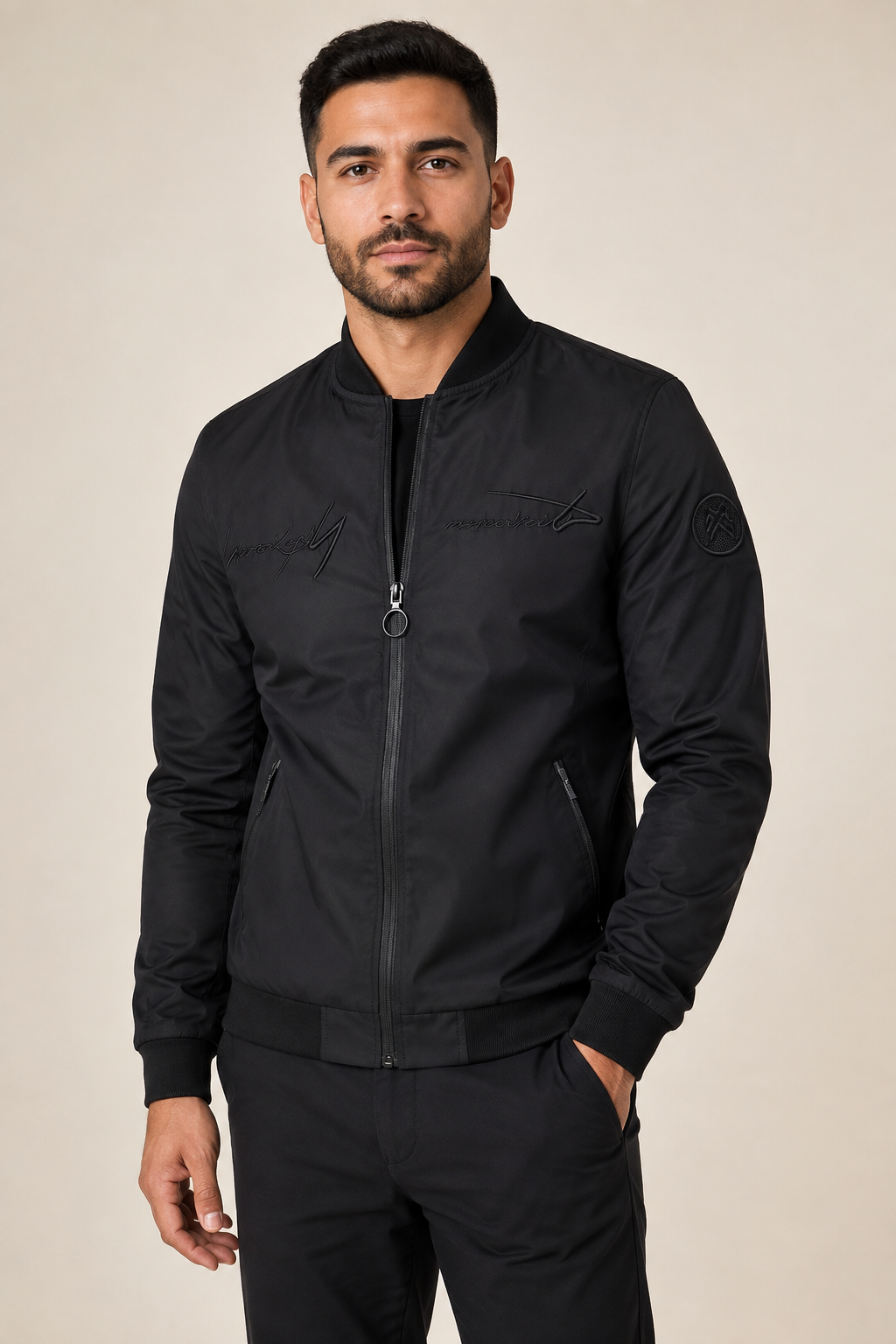Men's black embroidered bomber jacket, worn by model in warm beige studio