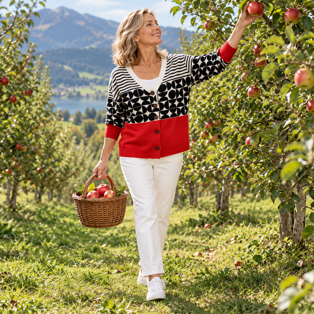 Strickjacke Raphaëlle im Apfelgarten beim Apfelpflücken, Ganzkörperansicht.