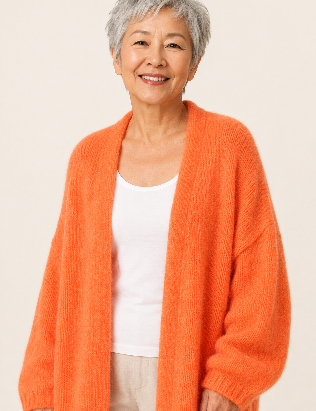 Lidia orangefarbener langer Oversized-Cardigan an reifer Frau auf warmem beigem Hintergrund