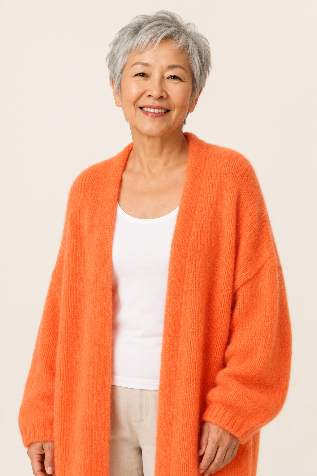 Lidia orangefarbener langer Oversized-Cardigan an reifer Frau auf warmem beigem Hintergrund