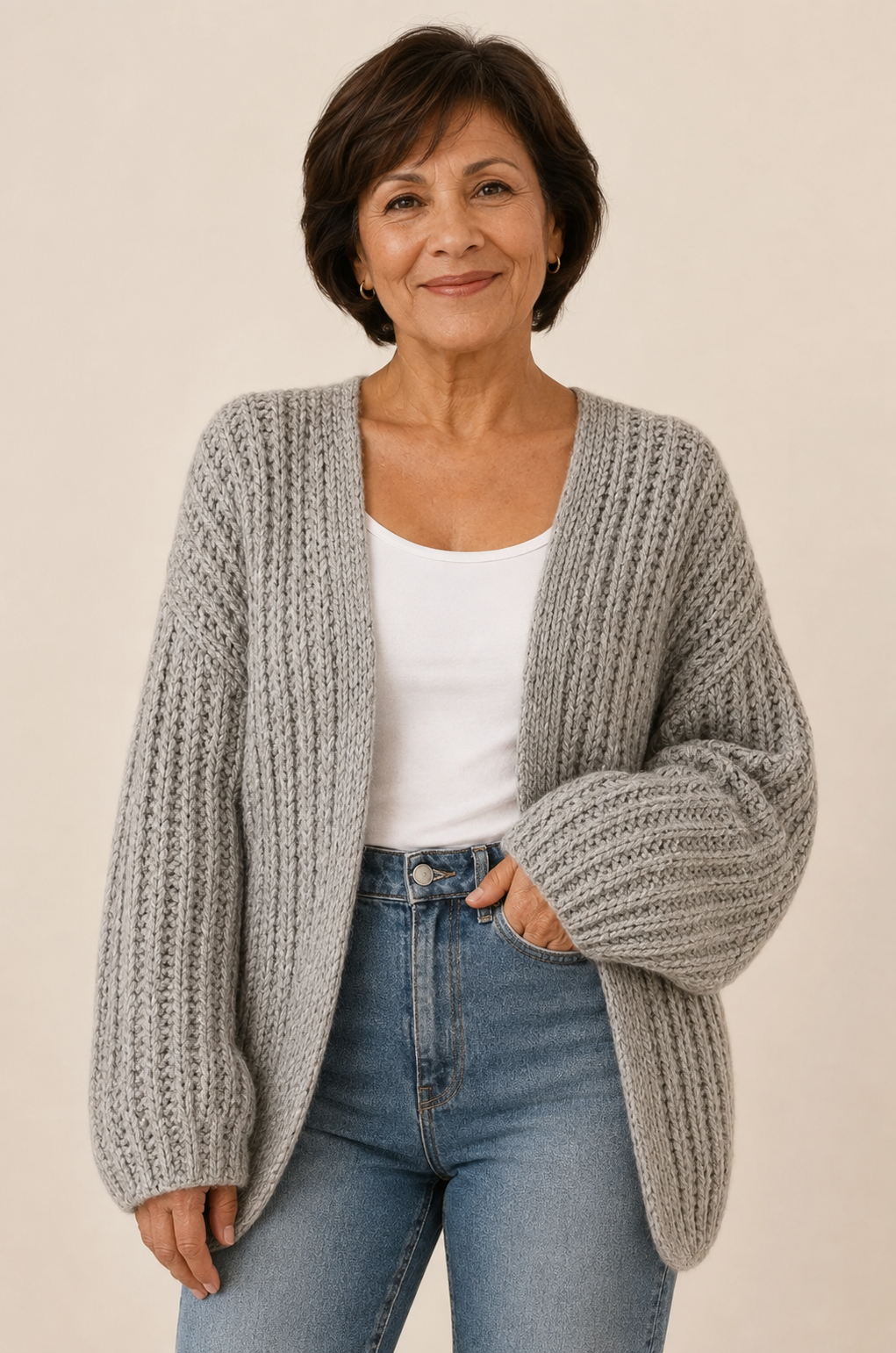 Graue Strickjacke mit Oversize-Ärmeln an reifer Frau auf warmem beigem Hintergrund